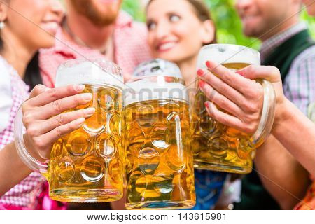 Five friends, men and women, having fun in beer garden clinking glasses with beer