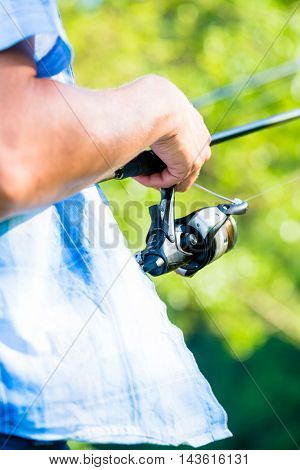 Close shot of sport fisherman reeling in the line on his fishing rod