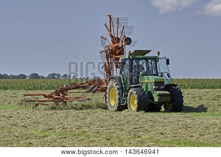 YSBRECHTUM, THE NETHERLANDS - AUGUST 22, 2016: A green tractor with a Kuhn rotary rake using one rotor for making small windrows for quicker drying of the hay.