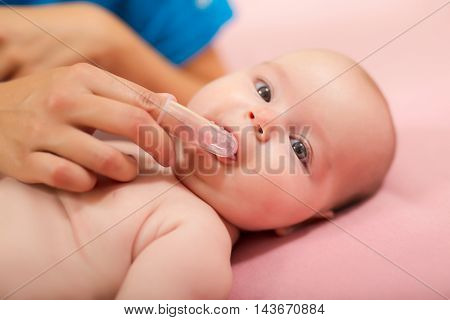 Mother cleaning baby`s mouth with special fingertip brush for children
