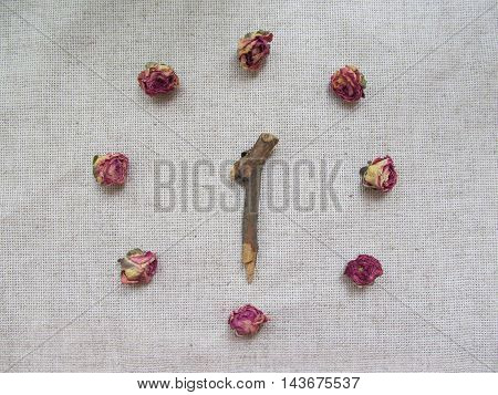 Clock made from dry rose buds and stick on linen background