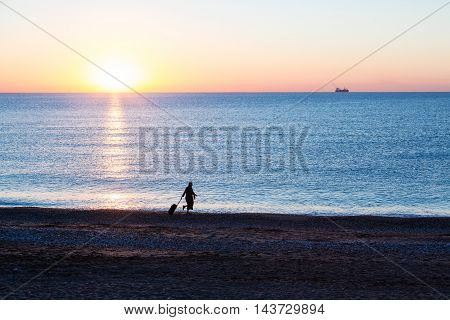 Exotic Vacation Silhouette of Female pulling Travel Suitcase along Ocean Beach Luminous Sunrise on Background