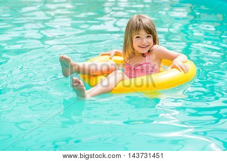 Happy little girl floating in the pool to rescue circle yellow