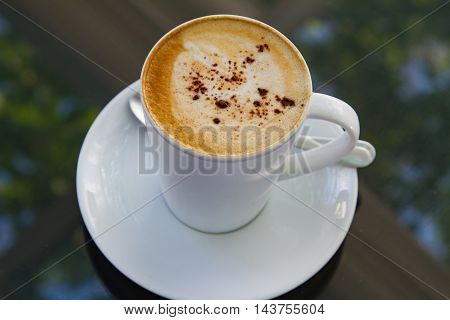 A cup of coffee in a white cup on glass background