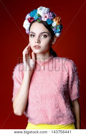 Beautiful model with a wreath of flowers on her head on red background