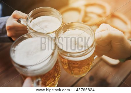 people, leisure and drinks concept - close up of male hands clinking beer mugs at bar or pub