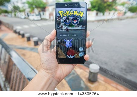 Penang, Malaysia - August 13, 2016 : Man holding a smartphone with his left hand playing Pokemon Go game. Screen on the smartphone is a Pokemon character called 