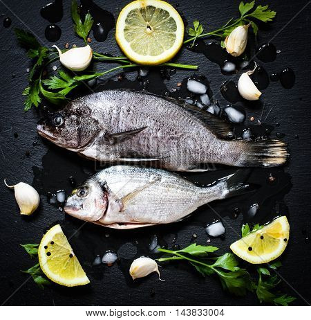 Fresh Fish Orata Over a Black stone with vegetables, lemon and pieces of ice. 