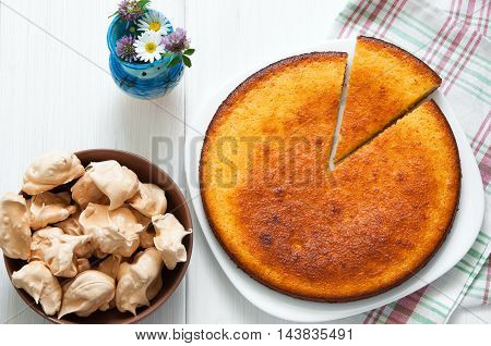 Top view: flowers, brown meringues and manna semolina pie on white wooden table