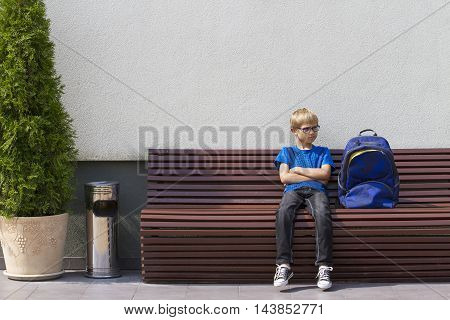 Boy with glasses sitting on the bench and waiting. Outdoors