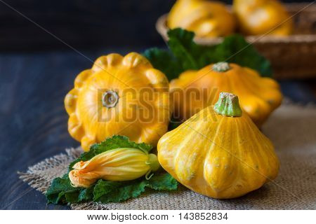 three yellow pattypan squash with leaf and flower on a dark wooden table.