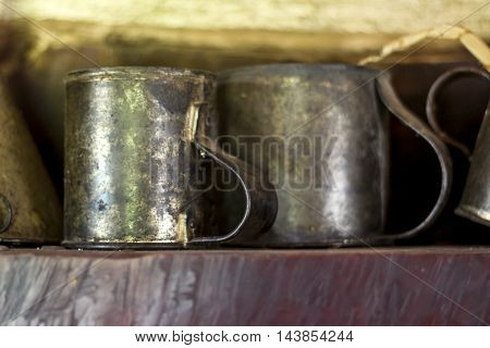 Antique tin cups sit on shelf in wooden cottage.