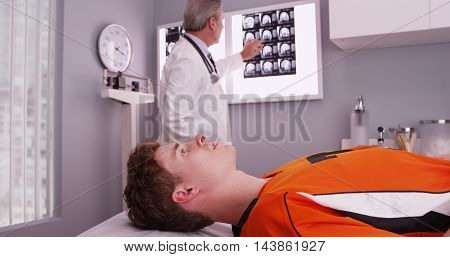 Portrait Of Young Sports Athlete Lying Down While Doctor Reviews Xrays