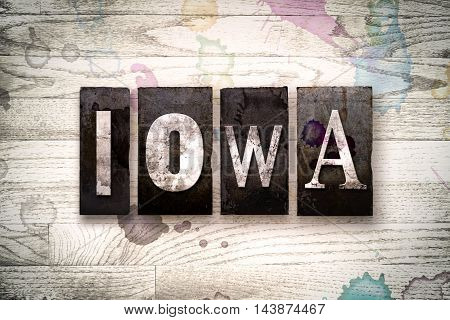 The word "IOWA" written in vintage dirty metal letterpress type on a whitewashed wooden background with ink and paint stains.