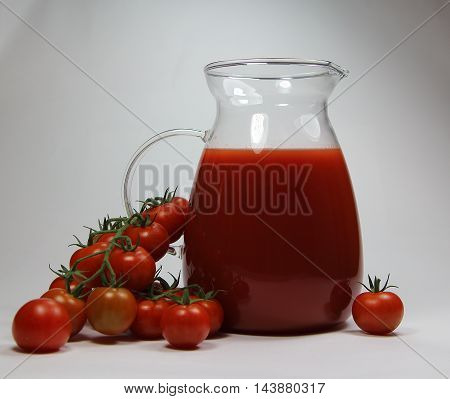 tomato juice in a jug with fresh tomatoes on a white table