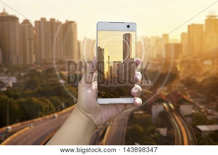 Hand holding white phone with city scape and wifi network connection concept .