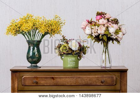 Three vases with colorful flovers on dresser in home inrerrior