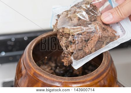 putting bag of herbal to an enamel pot to decoct herbal medicine