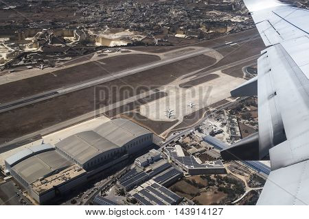LUQA, MALTA - AUGUST 06 2016: Aerial view of Malta airport runway and buildings. Shot taken inside departing commercial aircraft.