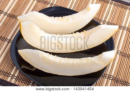 Slices of juicy melon on a black plate closeup on wooden background
