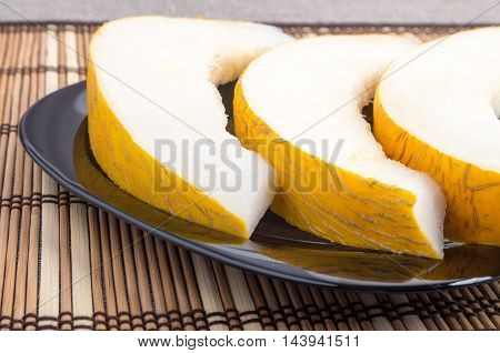 Three slices of juicy yellow melon on a black plate closeup on wooden background