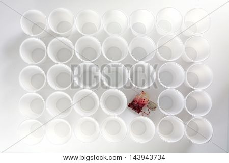 teabag with red hibiscus tea between ordinary rows of white plastic cups abstract clean art concept of social issues such as being different or consequences from staff shortening