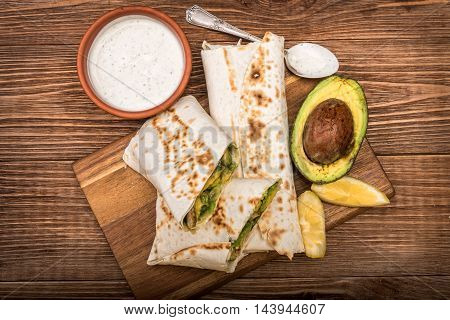 Chicken, avocado and vegetables burrito on the wooden background.