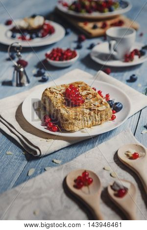 Sweet breakfast with pastry pie and berries - cowberry, red currant and bluberries. Beautiful food served at blue rustic wooden table, cake dessert at white porcelain plate, almonds and tea cup.