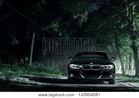 Saratov, Russia - June 12, 2015: Black car BMW E90 stand on road in darkness forest at night