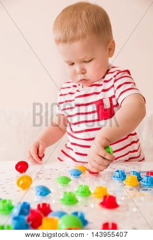 Closeup of child's hand taking bright mosaic parts. Playing and learning colors at home. Toddler boy in a striped shirt playing with colorful constructor details. Activities with children