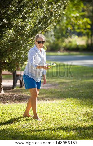 Girl having fun with frisbee in the park. Sunny summer day. Outdoor shot. Woman tossing a frisbee. Woman in sunglasses throwing a flying disc in a summer day.