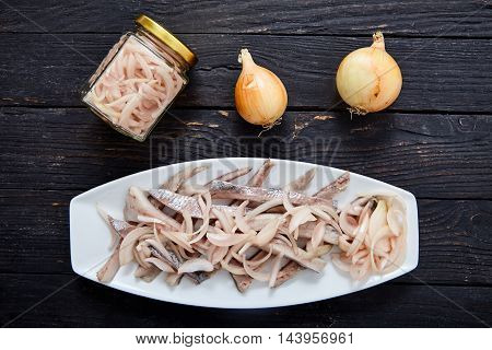 Top view of sliced herring fillets with cutted into shreds onion marinated in vinegar on white plate. Traditional home cold appetizer on wooden background with fresh onions and pickled onions in jar