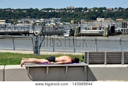New York City - August 29 2011: Man sunbathing on a bench in Hudson River Park North at West 125th Street