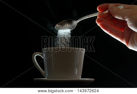 hand pouring brown sugar in white cup of coffee