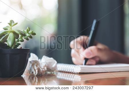 Closeup Image Of A Hand Working And Writing Down On A White Blank Notebook With Screwed Up Papers On