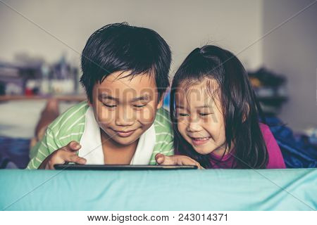 Asian Children Playing Game On Digital Tablet Together. Chinese Boy And His Pretty Younger Sister Sm