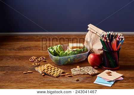 Back To School Concept, School Supplies, Assortment Of Biscuits And Transparent Lunchbox Full Of San