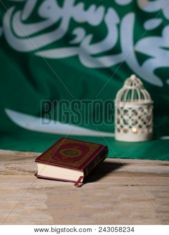 Sacred Book Of Koran On A Wooden Surface. Saudi Arabian Flag In The Background