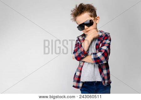 A Handsome Boy In A Plaid Shirt, Gray Shirt And Jeans Stands On A Gray Background. The Boy In Black 