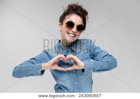 Young Girl In Black Cat Glasses On A Gray Background. Portrait Of A Young Beautiful Girl. Charming G