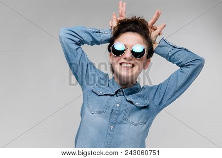Young Girl In Round Glasses On A Gray Background. Portrait Of A Young Beautiful Girl. Charming Girl 