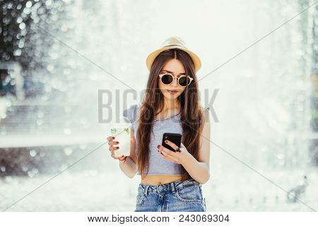 Young Happy Woman In Sunglasses And Summer Hat Sefing In Internet From Phone On The Street With Cock