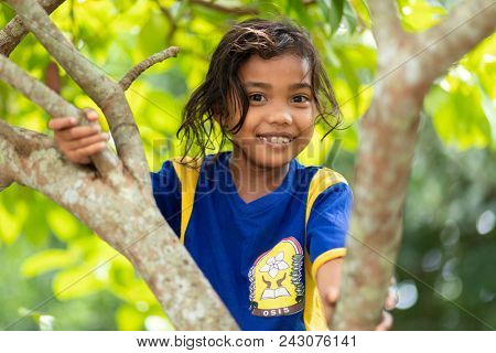 BANDA NEIRA, MALUKU ISLANDS, INDONESIA, DECEMBER 17, 2017 : Portrait of a smiling sweet little girl climbing at a tree in Banda Neira, Maluku islands, Indonesia.