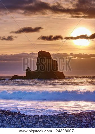 Sea Stack Sharp Silhouette By Sunset Sky. Evening Light On The Rocks, Boulders And Cliff Face Of Tal