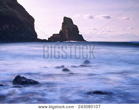 Cloudy Evening On Rocky Shore At Sunset. Sunset Mirroring In  Sea Water And Large Cracked Rocks With