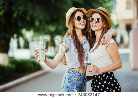 Happy Positive Moments Of Two Stylish Girls Hugging With Cocktails On Street In City. Closeup Portra