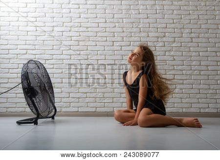 Little Girl Struggling With Heat And Sitting In Front Of A Fan With Flying Hair In An Apartment On A