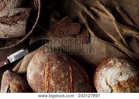 Elevated View Of Various Types Of Bread, Knife, Wicker Breadbasket On Sackcloth