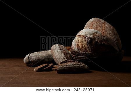 Closeup Shot Of Various Types Of Bread And Wicker Breadbasket On Wooden Table Isolated On Black Back
