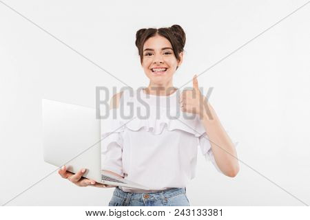 Photo of excited young woman with double buns hairstyle and dental braces on teeth holding laptop and showing thumb up isolated over white background